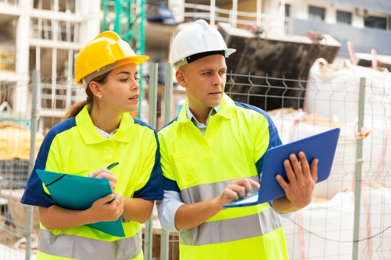 Two Qualified Engineers Working On A Construction Site Are Having a Discussion While Referring To A Mobile Computing Device